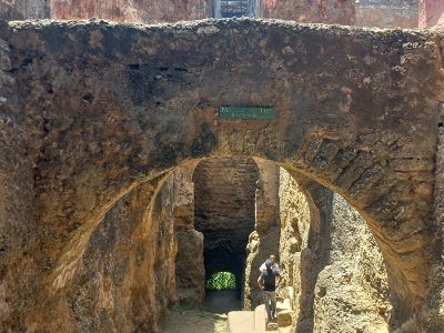 A photo of tourists exploring the historic Fort Jesus in Mombasa, Kenya, with the turquoise waters of the Indian Ocean in the background.