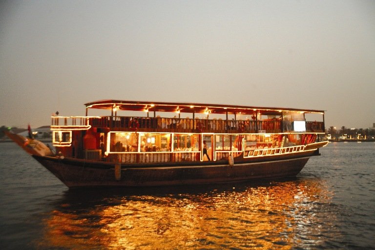 A beautifully decorated dhow sailing on the calm waters of Tudor Creek, Mombasa, with the setting sun in the background.